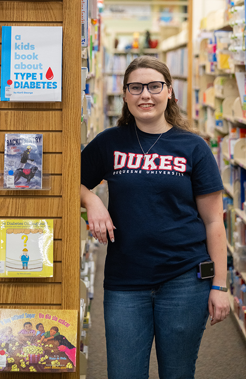 Hannah Litke standing next to "A kids book about Type 1 Diabetes" in Gumberg Library's Curriculum Center