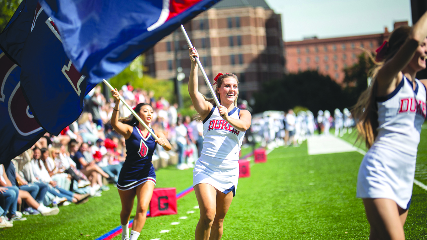 Duquesne University cheerleaders running on football field with flags