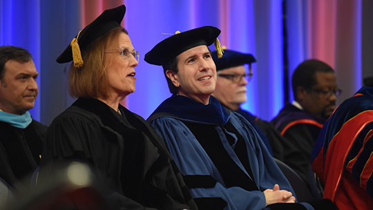 Two people wearing academic regalia and talking .