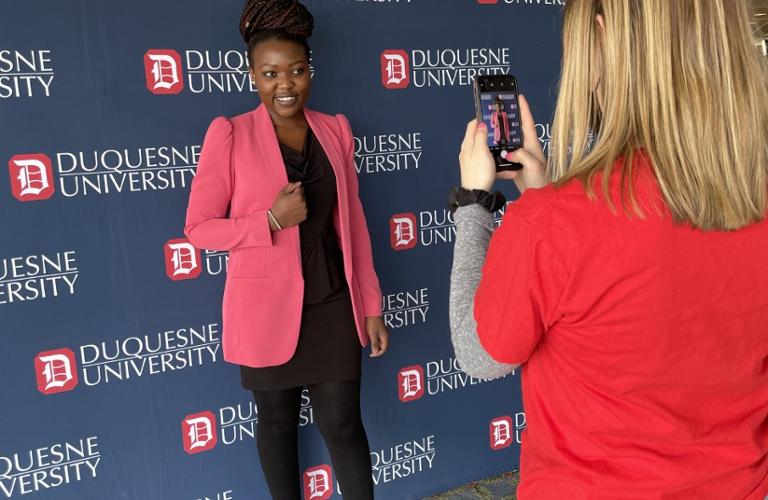 Student posing in professional attire in front of Duquesne University backdrop.