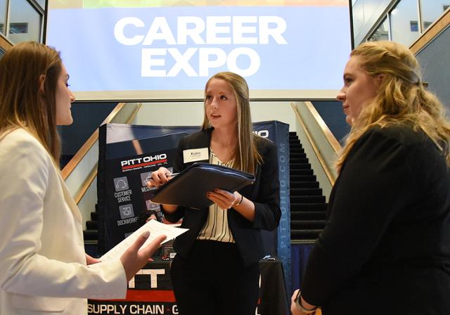 Three female students talking to one another in front of a Career Expo event sign.