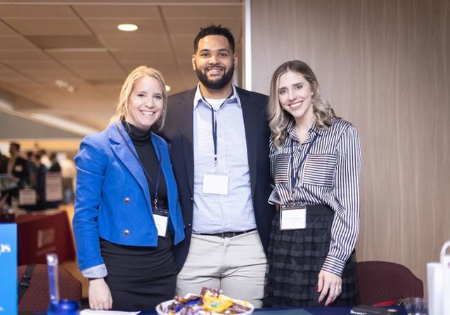 Three employers smiling behind a table at a previous career fair in the Union Ballroom