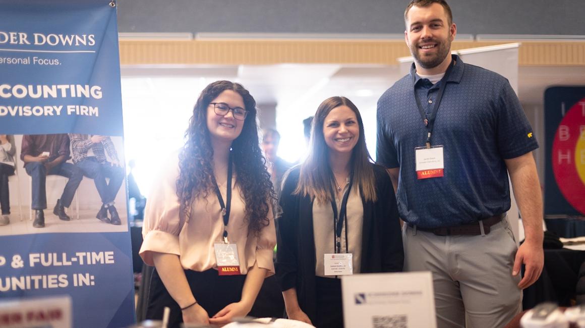 Three employers standing in front of the Schieder Downs banner at the campus Career Fair.