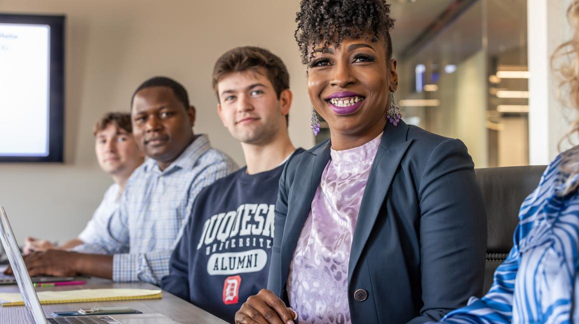 Graduate students sit in a conference room and smile.