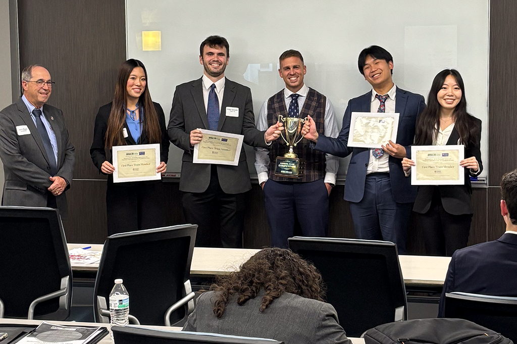 A group of professionally dressed students pose with certifcates and a trophy.