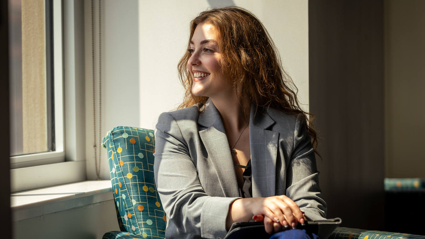 A graduate student looks out of a window and smiles.