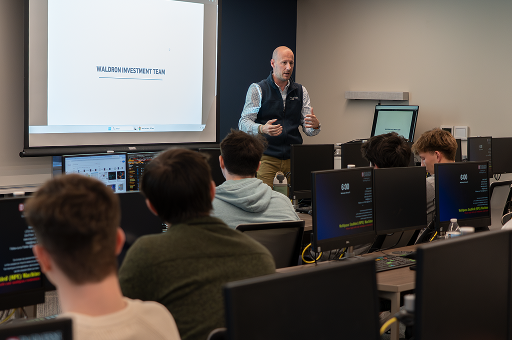 A finance professionals speaks to a group of students in an investment lab.