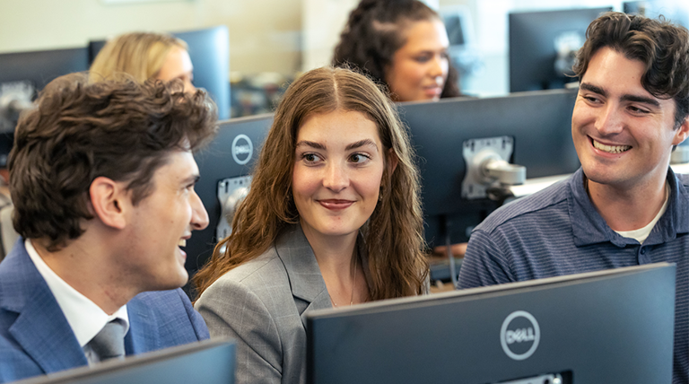 Students smile at each other in a computer lab.