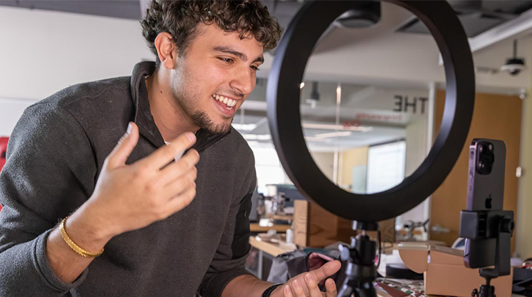 A marketing student films a video with an iPhone and ring light. 