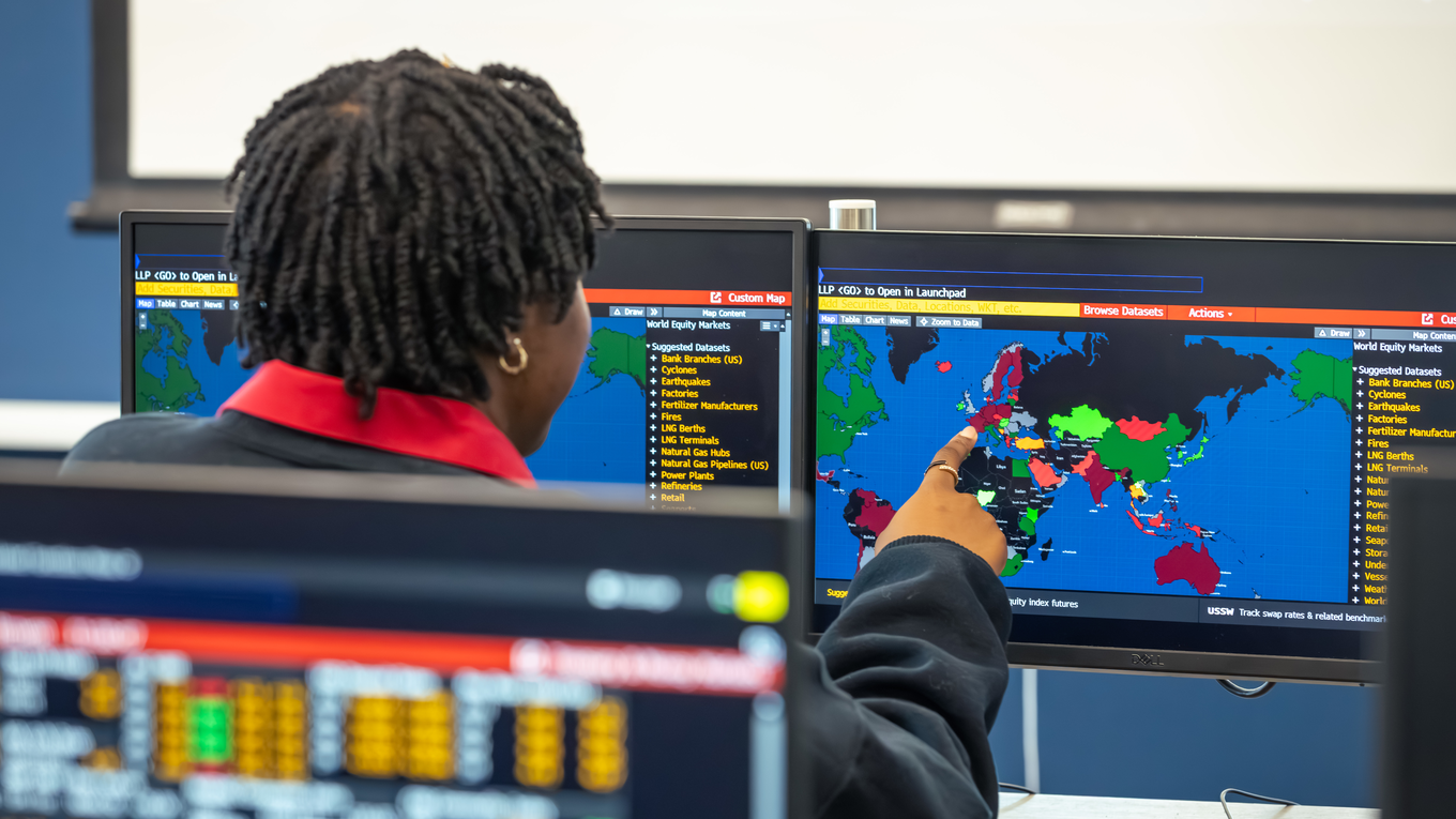 A student points at a world map on a computer screen.