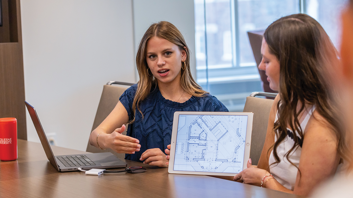A student shows a real estate blue print in a conference room.