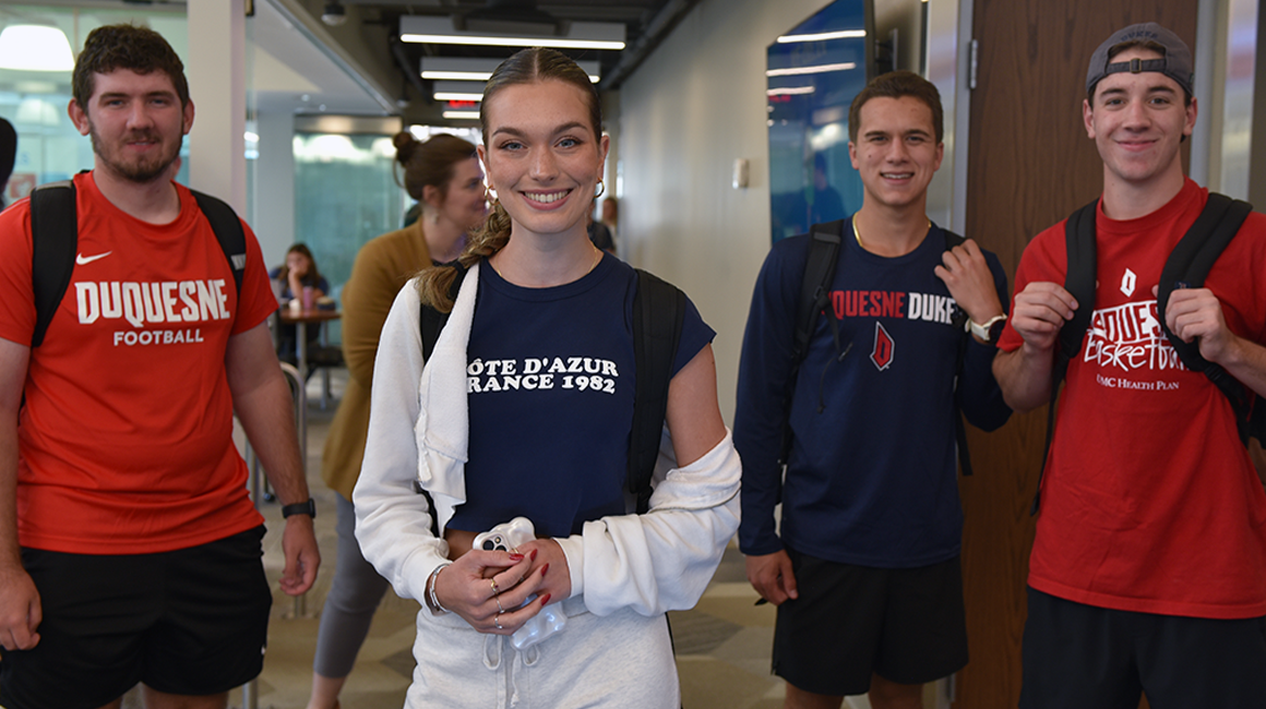 Smiling business students in Rockwell Hall wearing Duquesne gear.