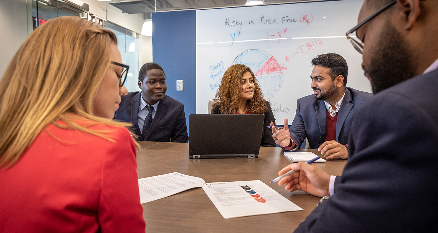 Business students talk while seated around a conference table.