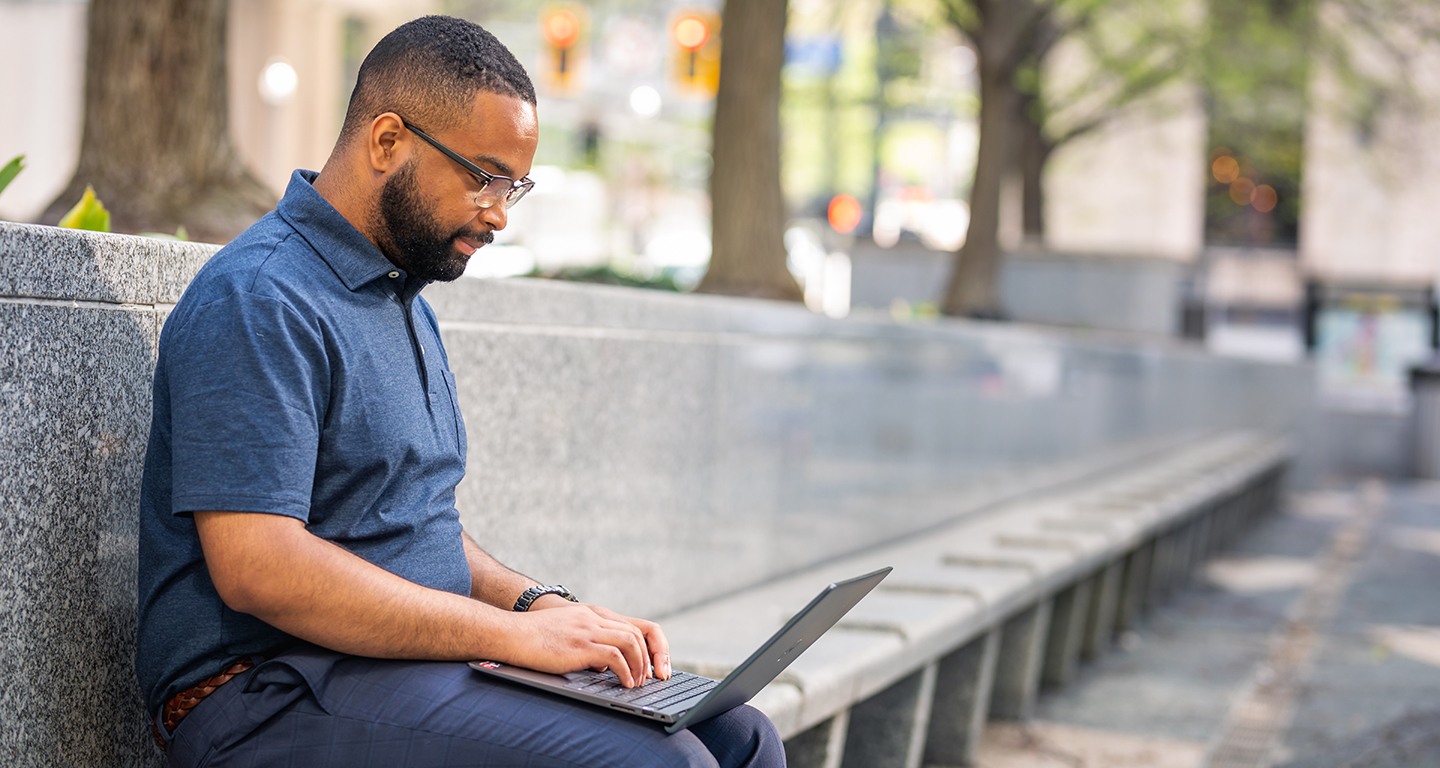 A business student works on his laptop while he sits outside. 