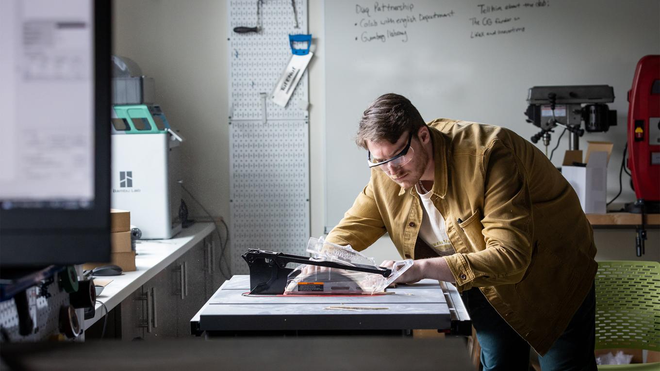 A business student operates a saw in a makerspace.