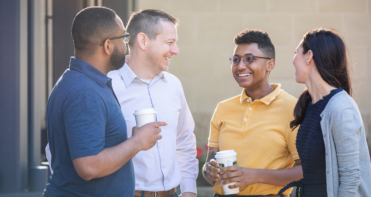 Four business students talk outside with coffee. 