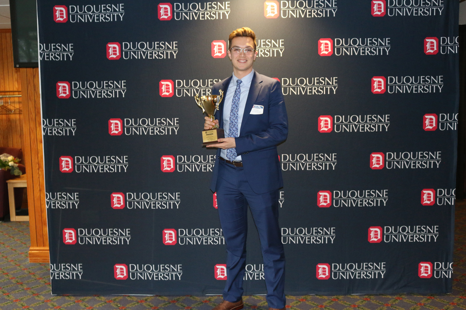 A business student holds a trophy in front of Duquesne University backdrop. 