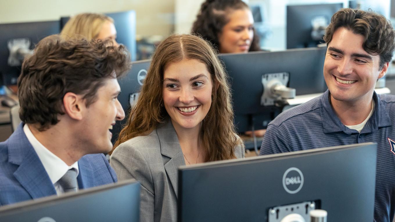 Students sitting in a computer lab look at eachother and smile.