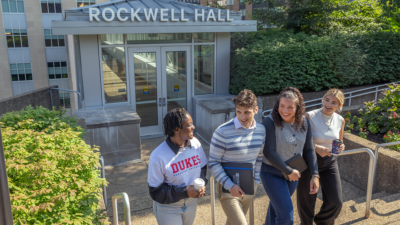 Students walk out of Rockwell Hall's entrance, smiling. 