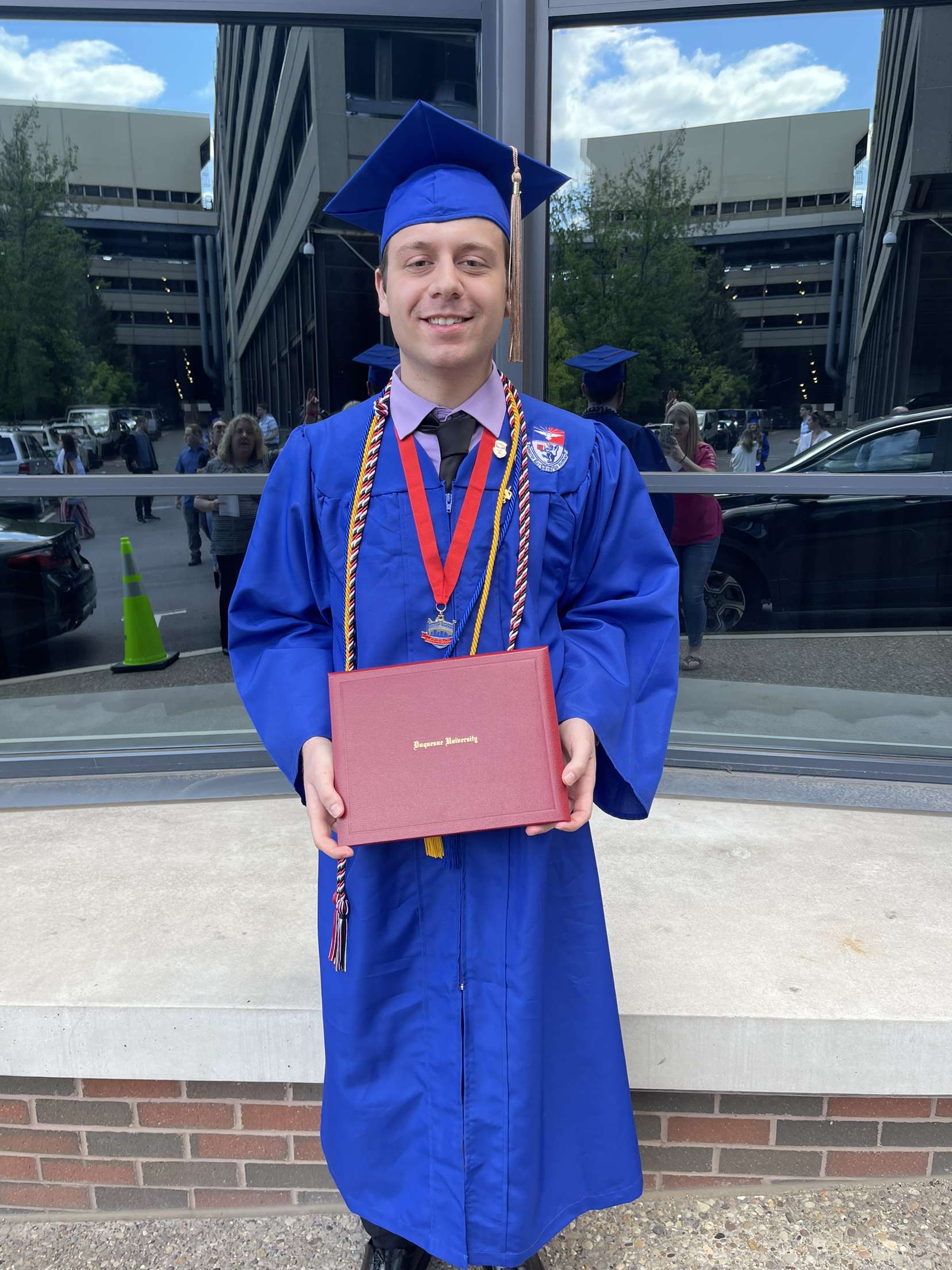 Jason Patrick posing with his diploma in his graduation robes. 