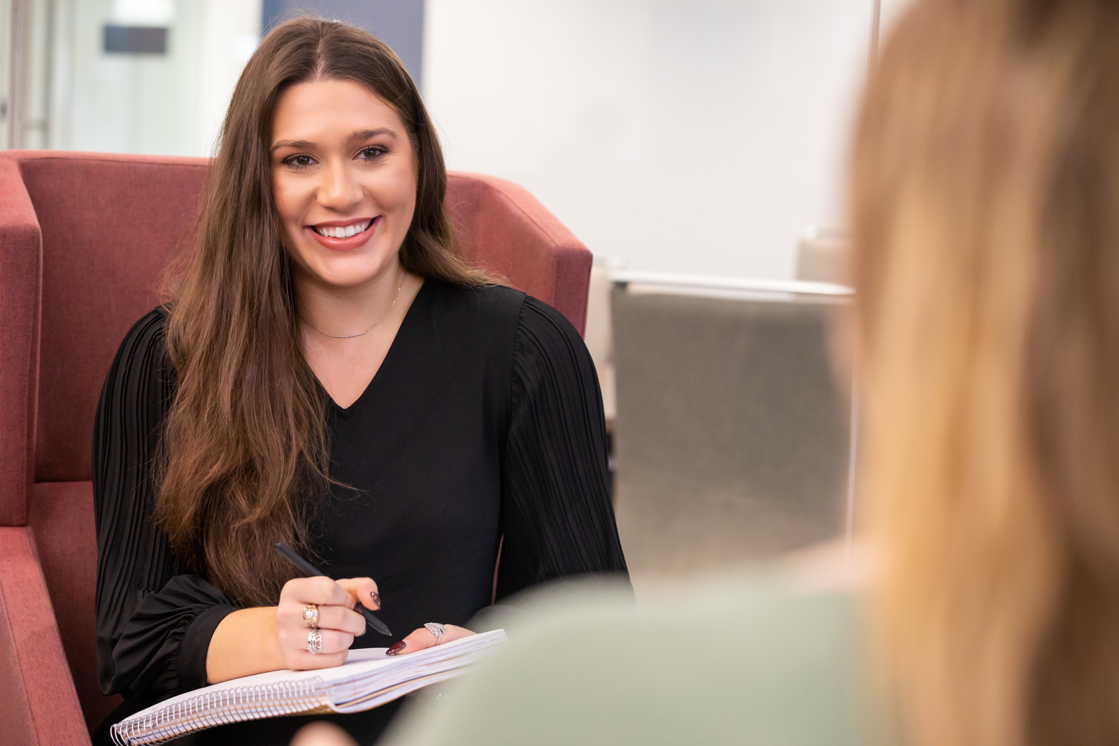 A seated business student smiles at another student. 
