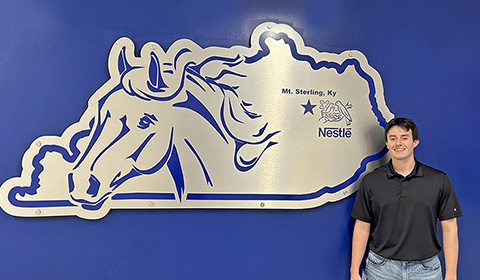 School of Business grad Ronnie Coleman, B'23, standing next to Nestle's Kentucky logo