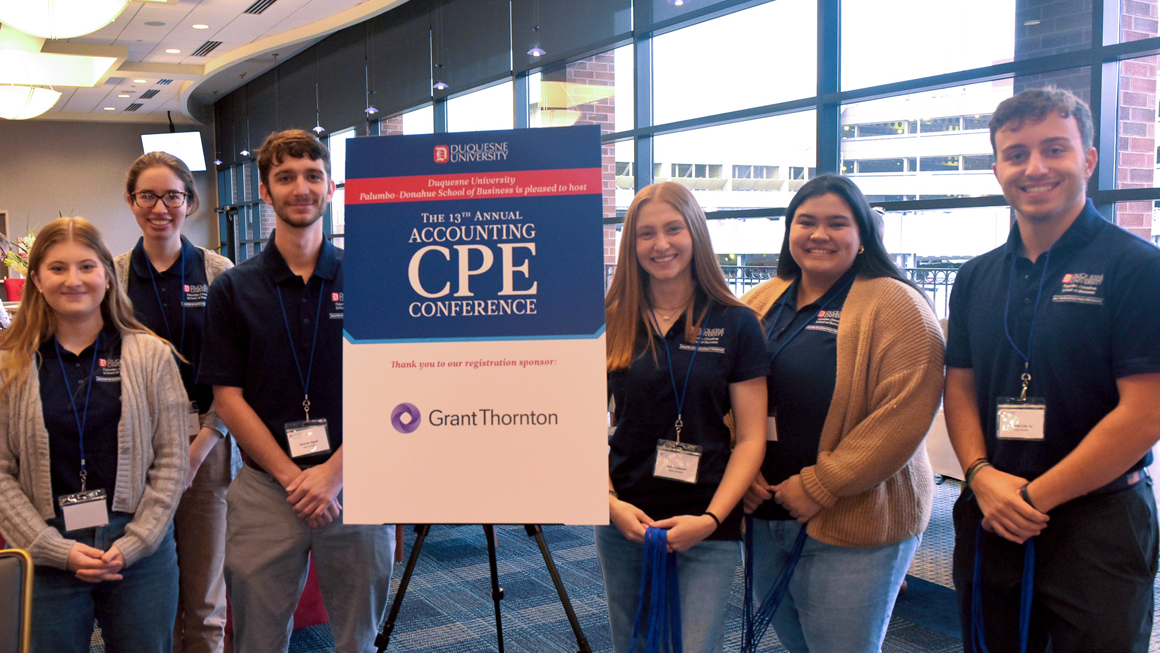Student volunteers pose in front of a Conference sign, wearing matching polos. 