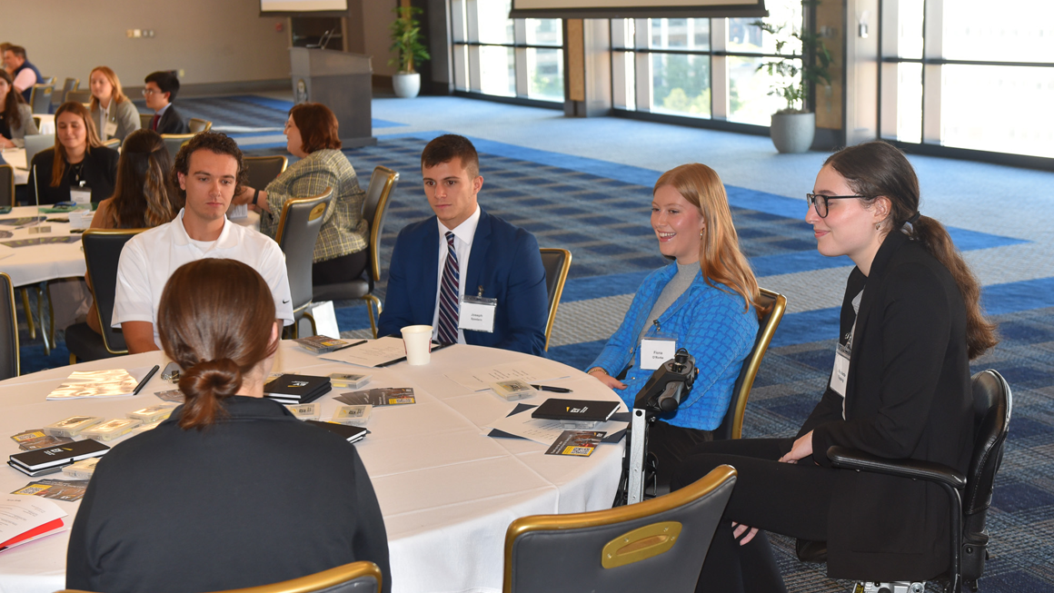 A group of students network with professionals. One of the students is smiling.
