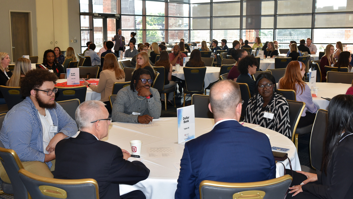 Students and professionals sit at tables and network. 