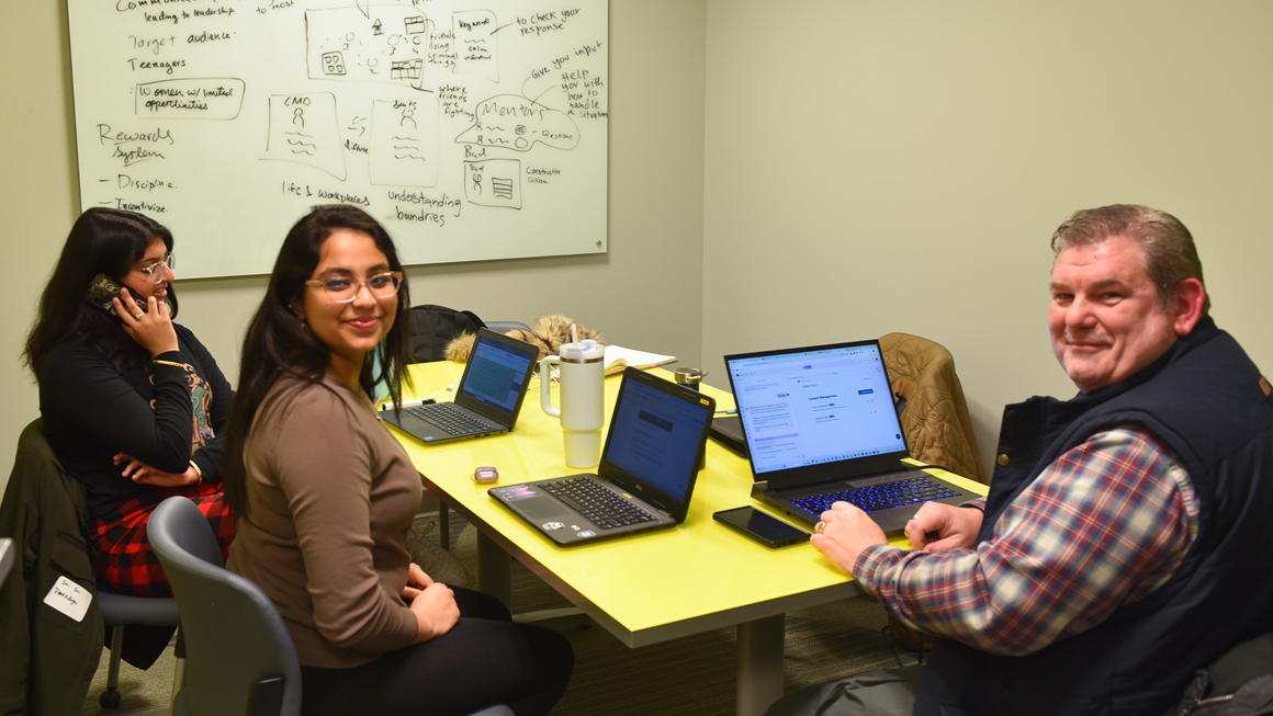 A team collaborates in a meeting room. There is a detailed brainstorm written on the dry erase board. 