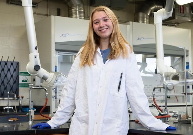 Madeline Sclichter standing in lab, wearing white lab coat.