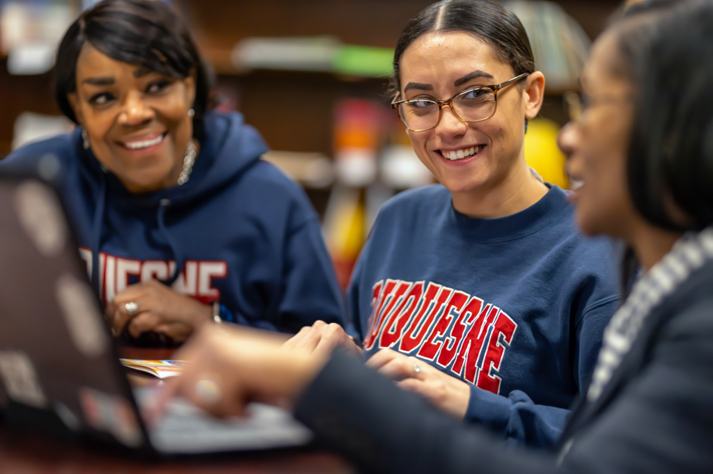 Duquesne Graduate School of Education student in center with laptop with other graduate program students on side collaborating on studies.