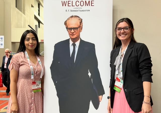 Graduate student Duaa Alzahrani and Dr. Reva Mathieu at conference for ABA work standing on either side of life-size B.F. Skinner poster