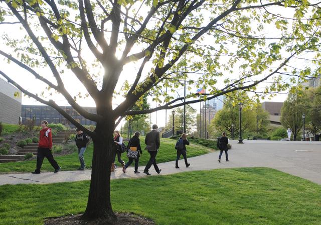 Duquesne admitted students walking on campus with tree in foreground and sunlight coming through in background