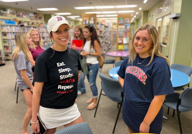 Two ambassadors smiling with prospective students & families in background in the Curriculum Center with Books and Puppets