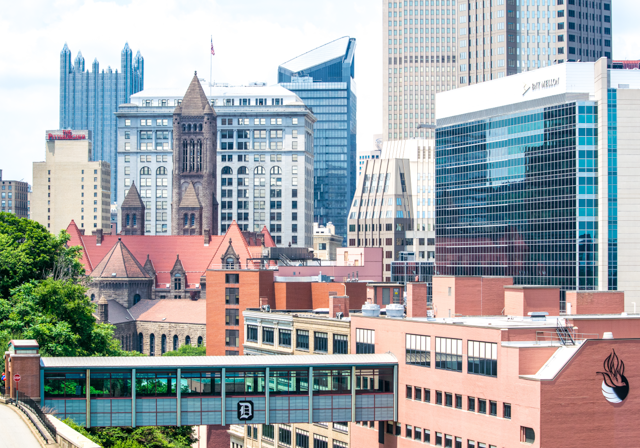 Cityscape from Duquesne's campus with university building in forefront and Pittsburgh skyline buildings in the background on a bright summer day