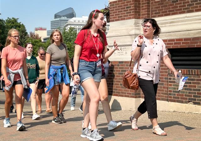 Prospective students and families on walking tour of campus by cornerstone of Canevin and cityscape in background