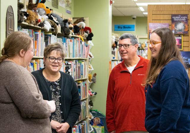 Admitted student with parents talking to staff in library Curriculum Center with color bookshelves and puppets in background