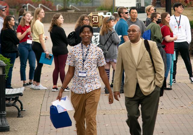 Father and son walking on campus during FAST summer event with other attendees in the background and Duquesne ring monument.