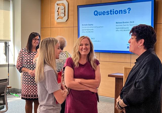 Junior preview day open house events with prospective students and families talking to faculty and staff in conference room with presentation screen in the background that says questions.