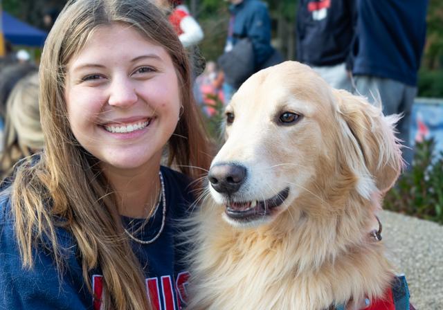 Duquesne student and dog selfie-style on campus event with crowd in background.