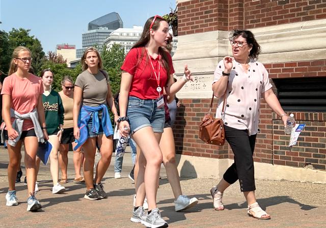 Students and parents walk on campus tour by Canevin Hall outside on campus smiling, conversing and walking during Summer Open House.