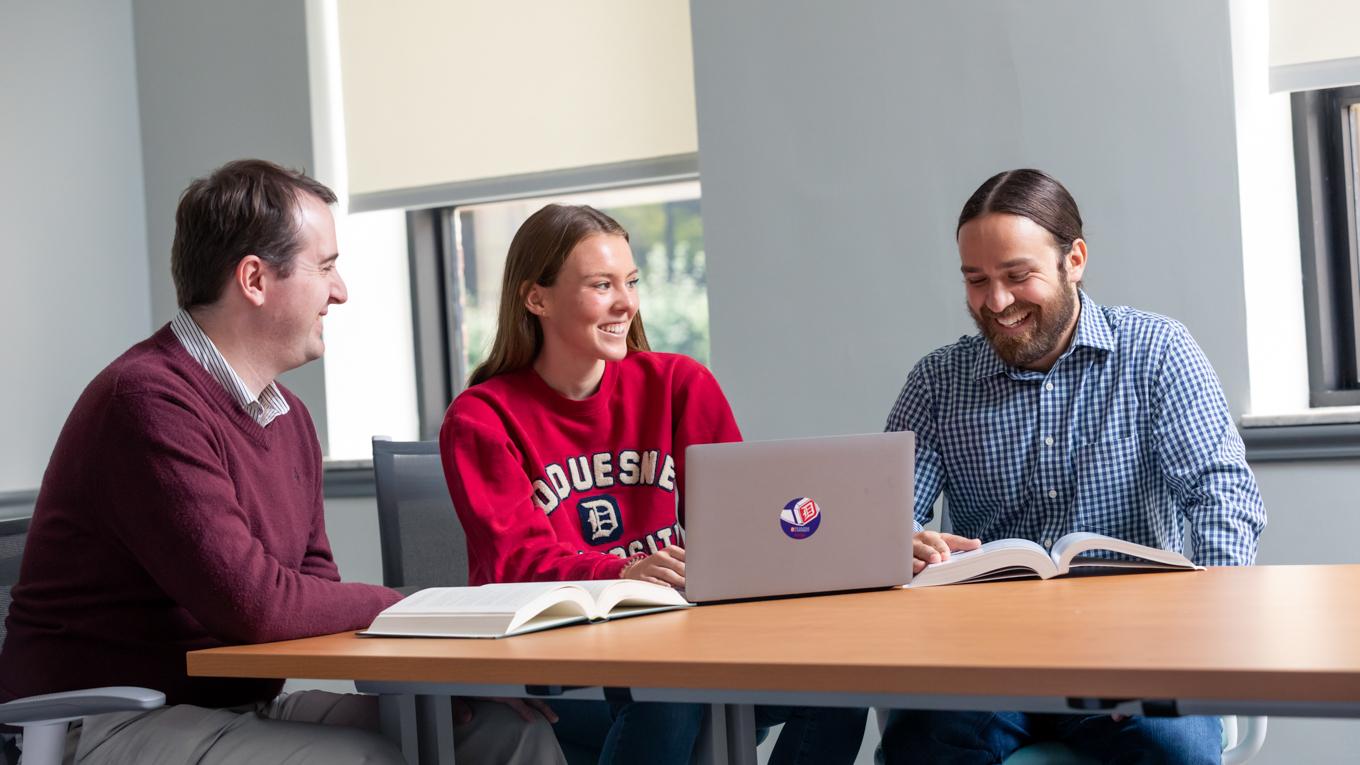 Duquesne students conversing around conference table with professor
