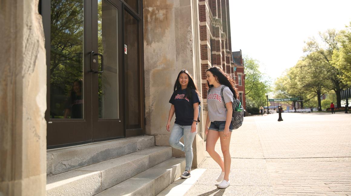 Two students on Academic Walk walking into Canevin Hall