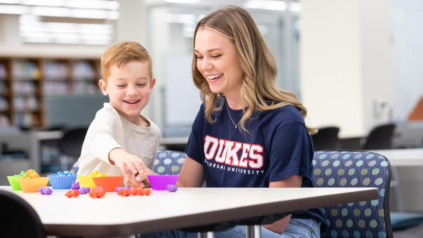 Duquesne student and young learning playing with colorful learning manipulatives at lbrary table