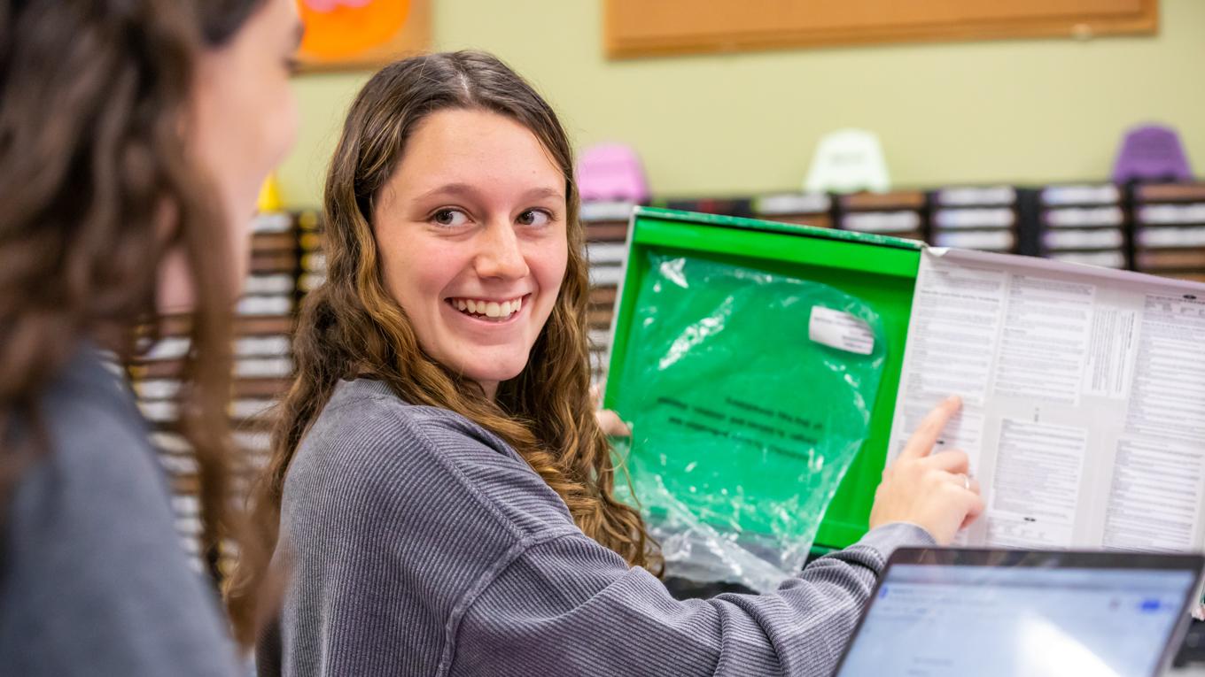 Image of Autism Endorsement student working with special education learning materials in library's curriculum center looking back and smiling at colleague