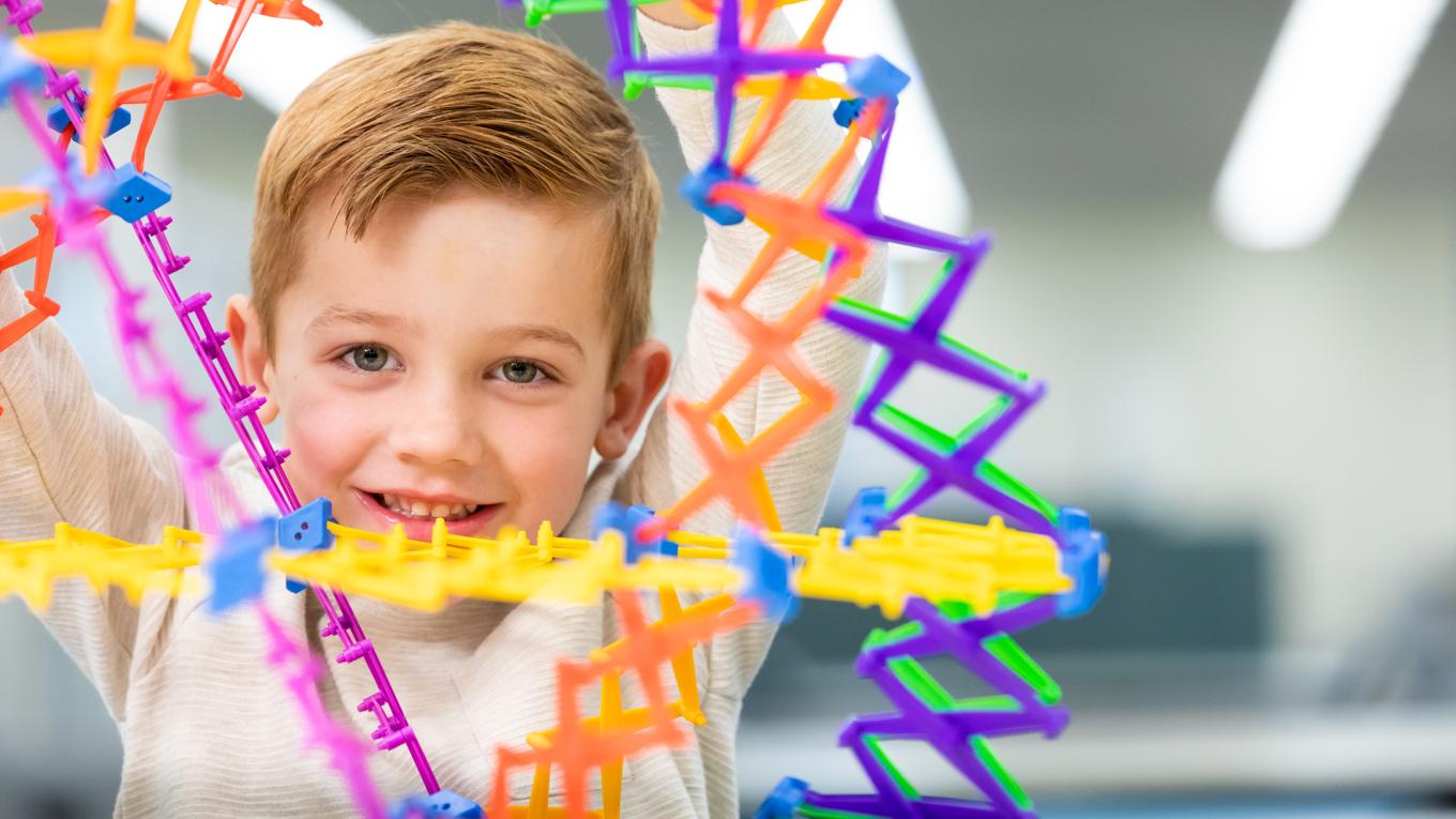 Young learner that Child Psychology student would work with is smilng looking ahead through geometirc globe learning manipulative for a behavior intervention as part of an IEP.