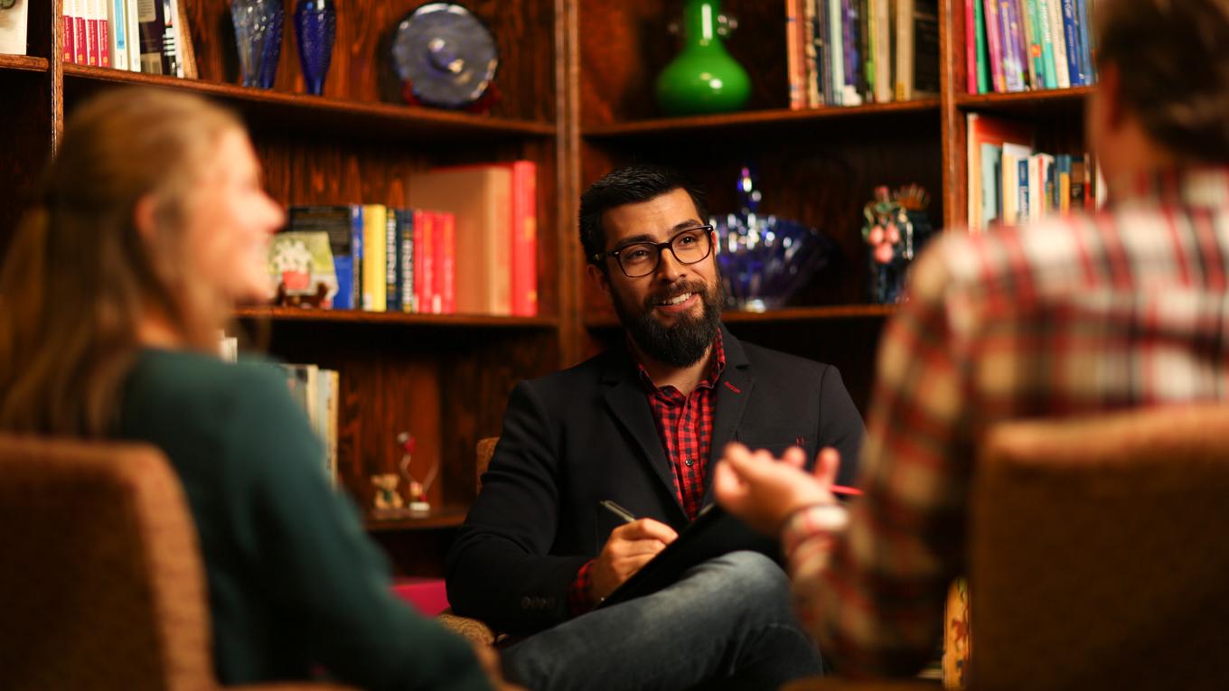 M.S. Marriage, Couple, and Family Counseling alum who is a counselor speaking with family clients in a private practice setting in a marriage counseling session.