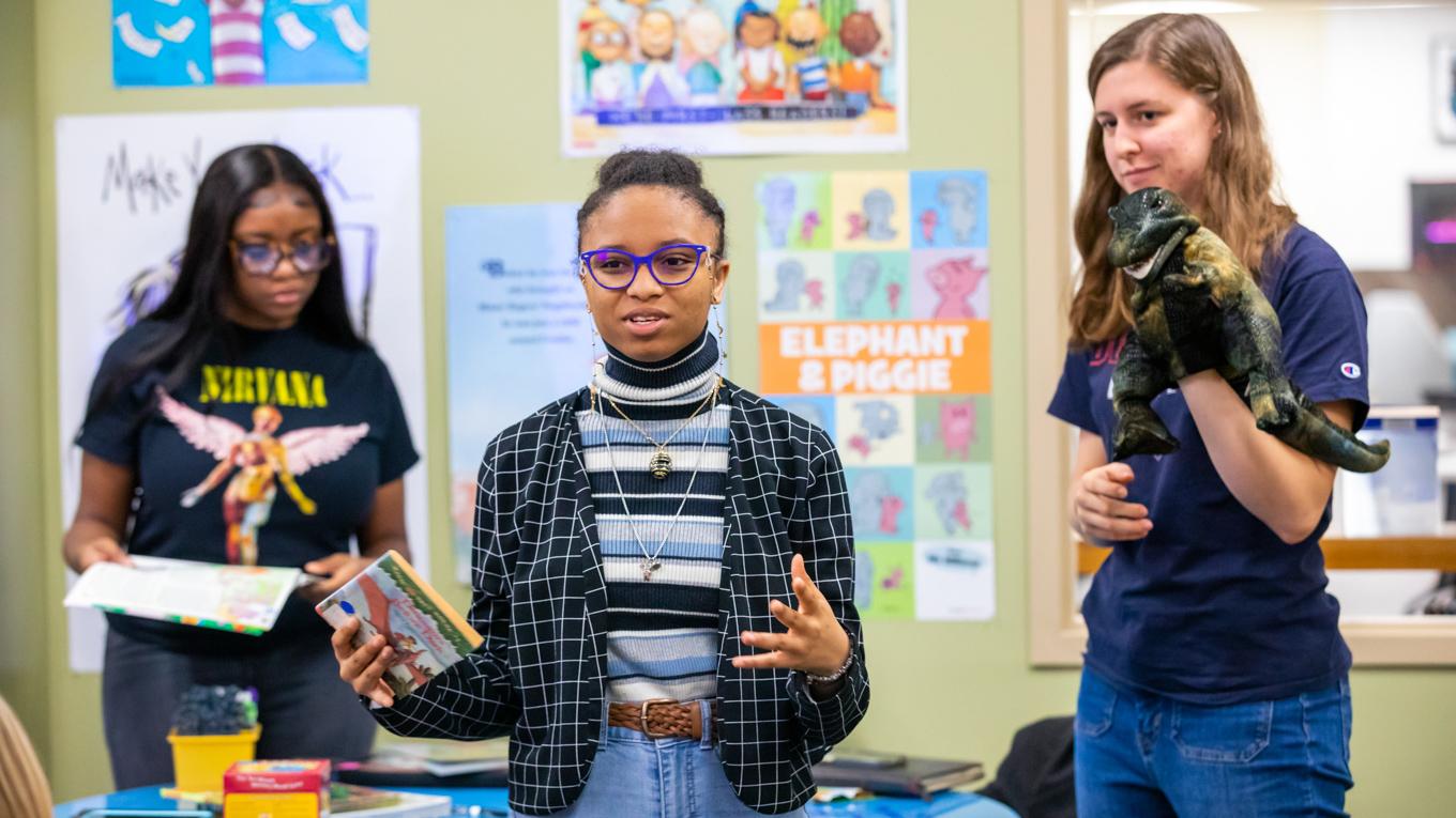 Three Duquesne students teaching prepared lesson in curriculum center with puppet, lesson plan, and book