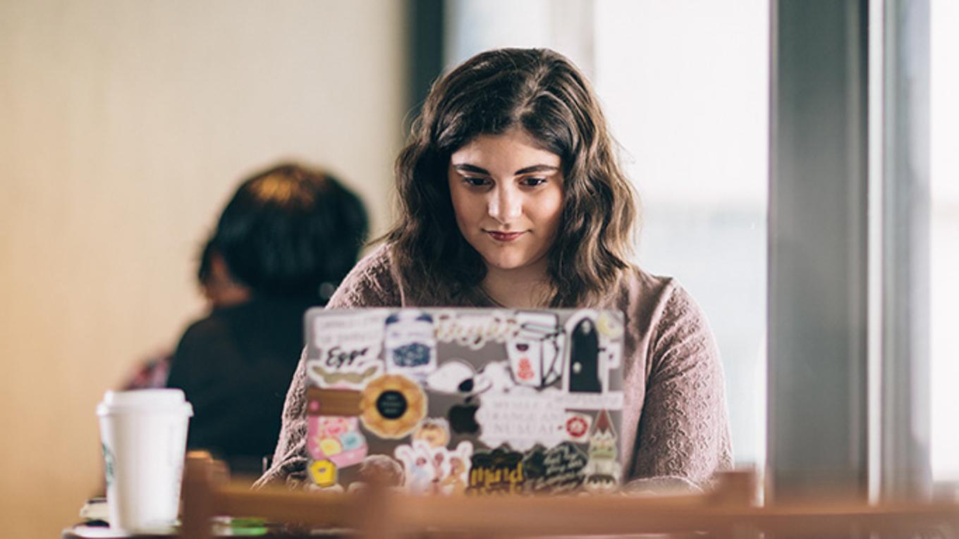 Higher education student studying at desk infront of laptop and with coffee at hand at university